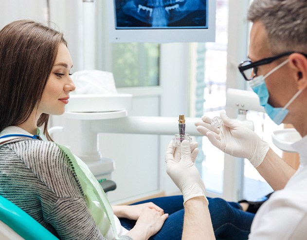 Dentist showing woman the parts of a model dental implant