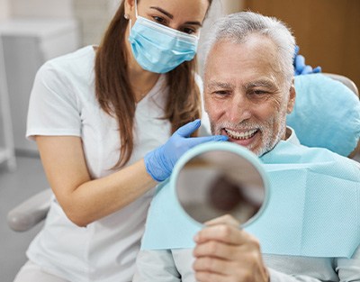 Dentist touching man’s teeth as he sits in dental chair looking at smile in mirror