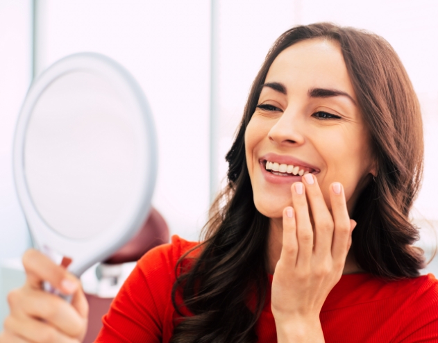 Woman admiring her new smile in mirror with dental implants in Castle Rock