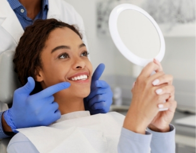 Woman in dental chair looking at her smile in mirror