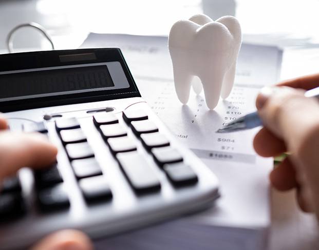 Hands holding pen and touching calculator at desk with invoices and large model tooth