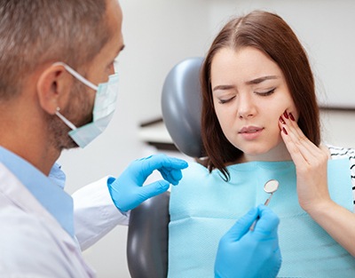 Woman with eyes closed touching cheek to show dentist where her toothache is