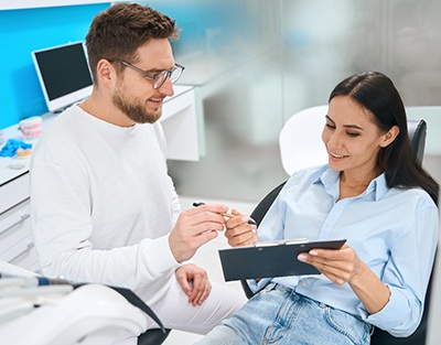 Woman in dental chair being handed financial forms on clipboard