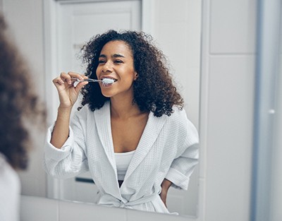 Woman brushing teeth in bathroom in front of mirror