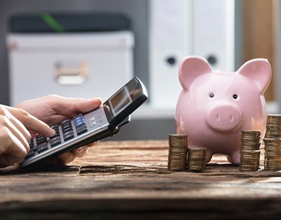 Pocket calculator is operated near piggy bank