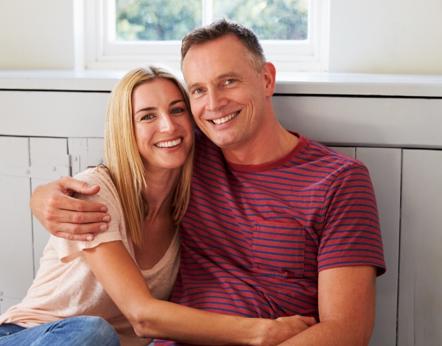 Smiling man and woman hugging after replacing missing teeth in Castle Rock