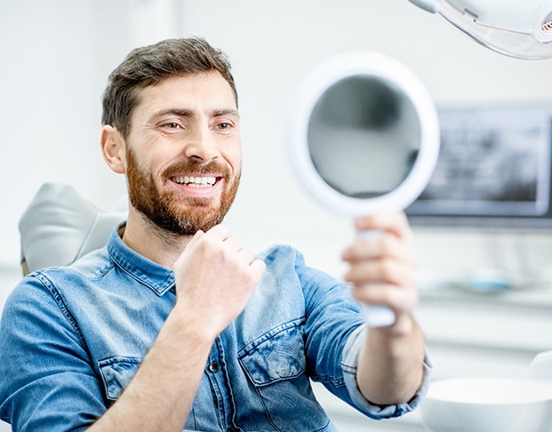 Man smiling at reflection in handheld mirror