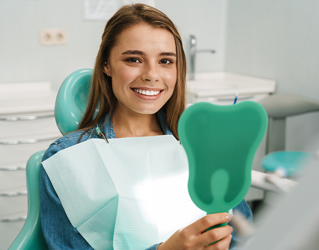 Smiling woman in dental chair holding a mirror